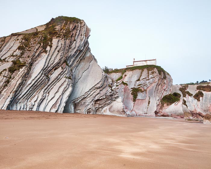 Flysch cliffs in the geological park at Itzurun Beach, with the Chapel of San Telmo on the cliff top, Zumaia, Basque Country, Spain.