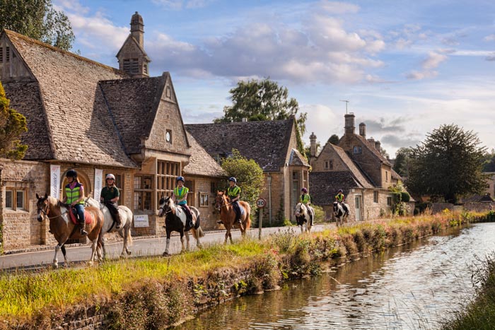 Group of girls riding horses through the Cotswolds village of Lower Slaughter, Gloucestershire, England