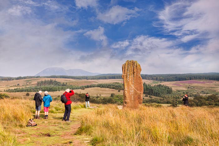 Tourists taking photos of one of the standing stones on Machrie Moor, Arran, North Ayrshire, Scotland.