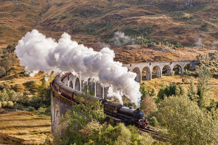 The Jacobite steam train blows steam from the exhaust as it crosses the Glenfinnan Viaduct, Highland, Scotland, UK.
