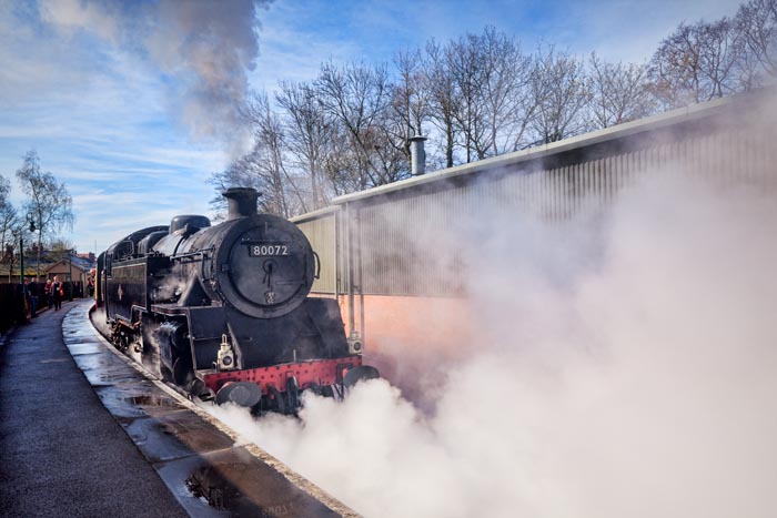 Tank engine 80072 of the North York Moors Railway blows off steam as it departs with a passenger train from Pickering Station in North Yorkshire, England, UK.