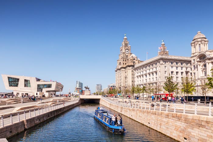 A narrowboat passing through the Liverpool Canal Link, in front of the Three Graces and the Mersey Ferries Building, Liverpool, England, UK