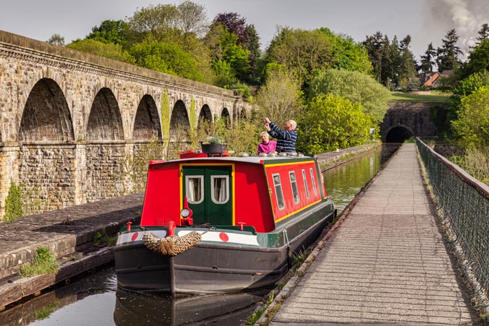 Senior couple in narrowboat crossing Chirk Aqueduct and taking photos of railway viaduct, Chirk, County Borough of Wrexham, Wales, UK
