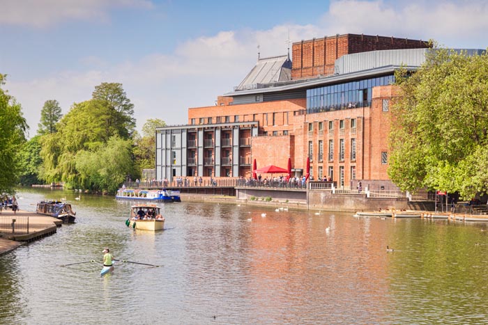Royal Shakespeare Theatre and the River Avon and people in boats on the river on a sunny weekend in late spring, Stratford-upon-Avon, Warwickshire, England, UK