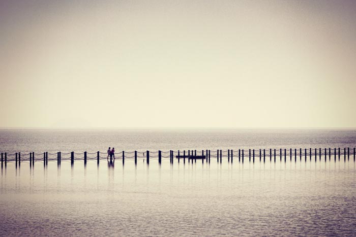Two people crossing the causeway which contains the Marine Lake between Knightstone Island and the mainland at Weston super Mare, Somerset, England, UK. Instagram type filter added.