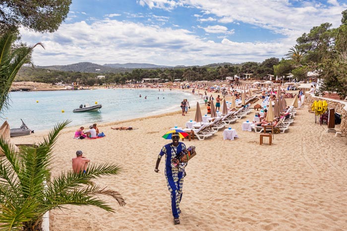 The beach at Cala Bassa, Ibiza, with beach vendor, known as looky looky man, approaching.