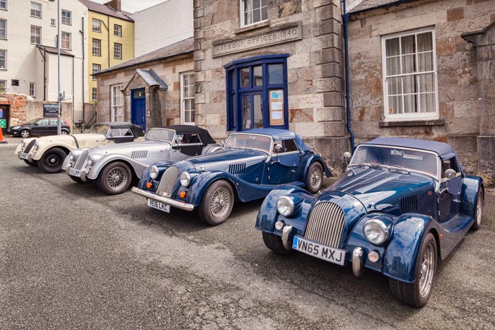 Four Morgan sports cars lined up in front of the Harbour Offices, Caernarfon, Wales, UK