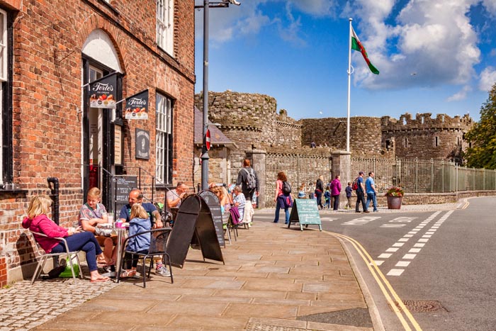 Holidaymakers at a pavement cafe in Beaumaris, Anglesey, Wales, UK, with the castle in the background.