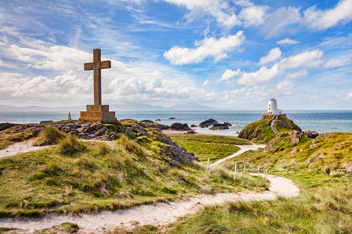 A large Christian cross and Twr Mawr, the old lighthouse on the tidal island of Ynys Llanddwyn, Newborough, Anglesey, Wales, UK