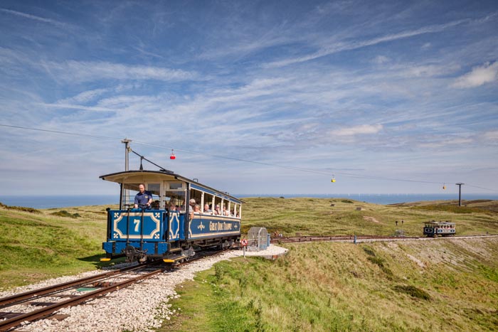 A passenger car of the Great Orme Tramway climbs from the upper passing loop as the descending car continues down, on Great Ormes Head, Llandudno, Conwy, Wales, UK. The Cable Car system is visible in the background.