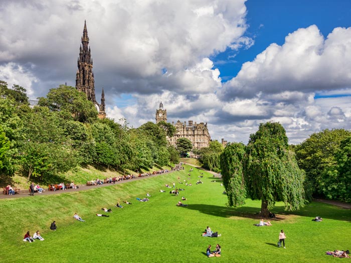 People sunbathing in Princes Street Gardens, Edinburgh, on a fine day in early autumn, with with Scott Monument and the Balmoral Hotel, Scotland, UK