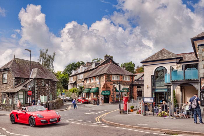 A red sports car driving through the village of Ambleside, Lake District National Park, Cumbria, England, UK