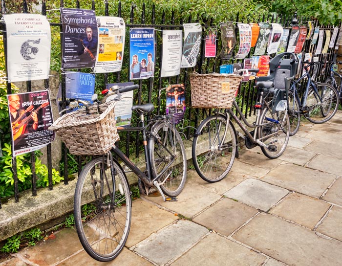 Cambridge bicycles leaning against a fence covered in posters, England, UK